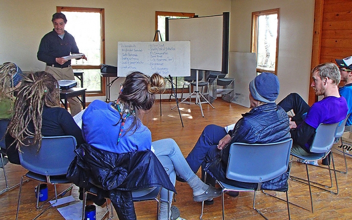 A group of students sit in chairs listening to an instructor during a wilderness first aid certification course. 